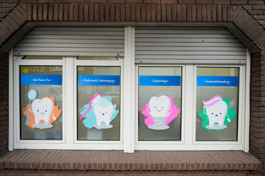 Fensterfront mit Illustrationen zu den Leistungen Anti-Karies-Kur, Zahnreinigung, Implantologie und Parodontalbehandlung