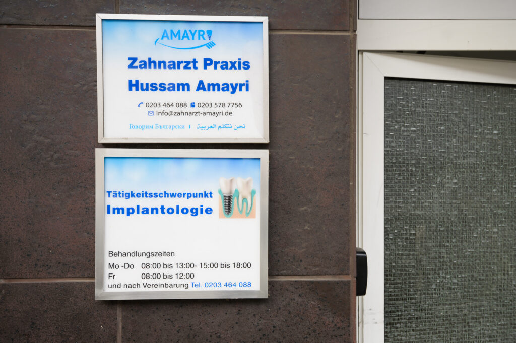 Praxisschild der Zahnarztpraxis Amayri mit Informationen, Öffnungszeiten und Schwerpunkt Implantologie